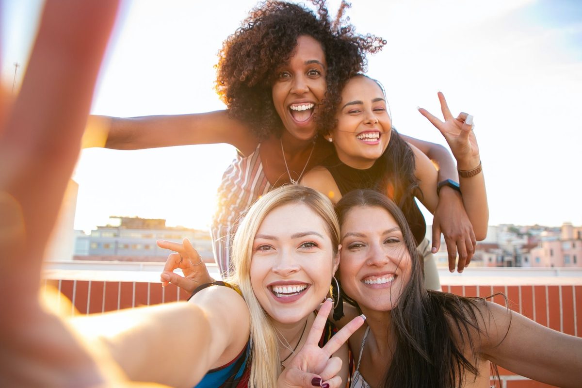 cheerful young diverse women showing v sign while taking selfie on rooftop